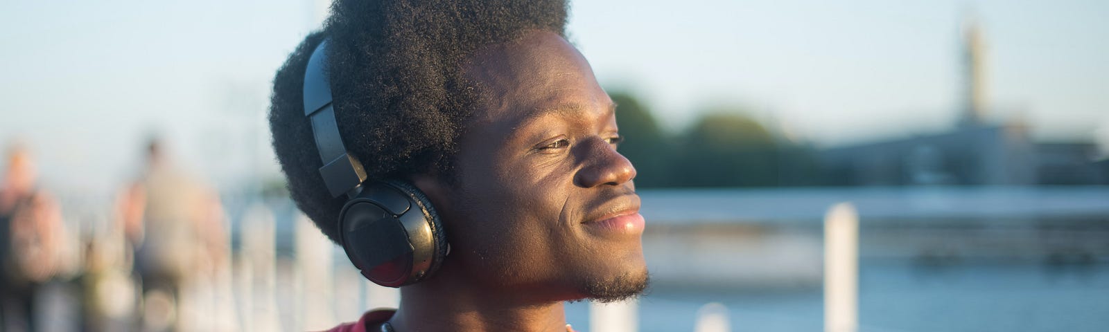 Young black man listens on headphones near water.