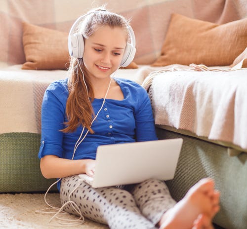 Young girl sits on the floor with a laptop and headphones.