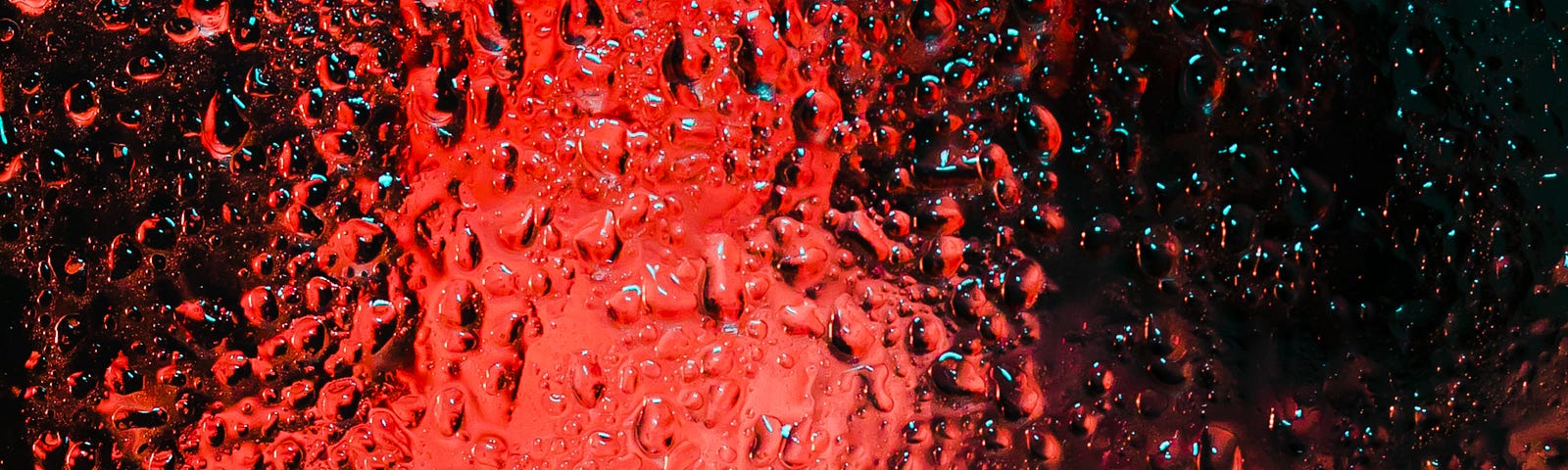 A window filled with droplets of water and red and turquoise light emanating from the other side.