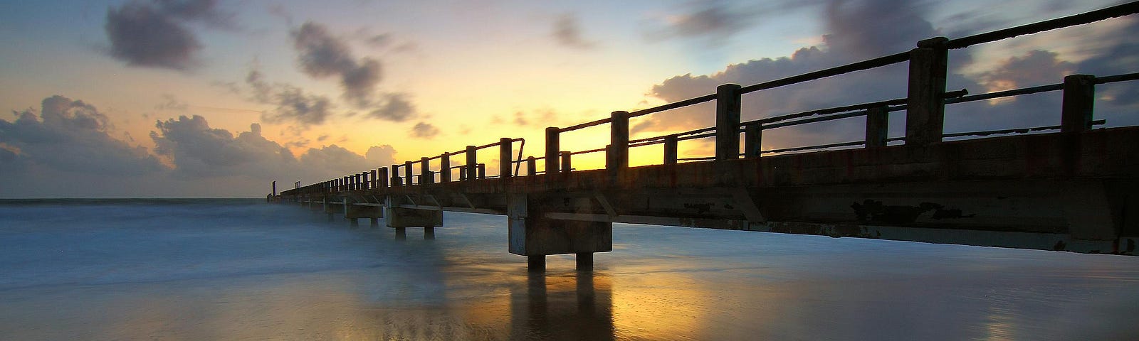 bridge stretching into the sunrise above a calm lake
