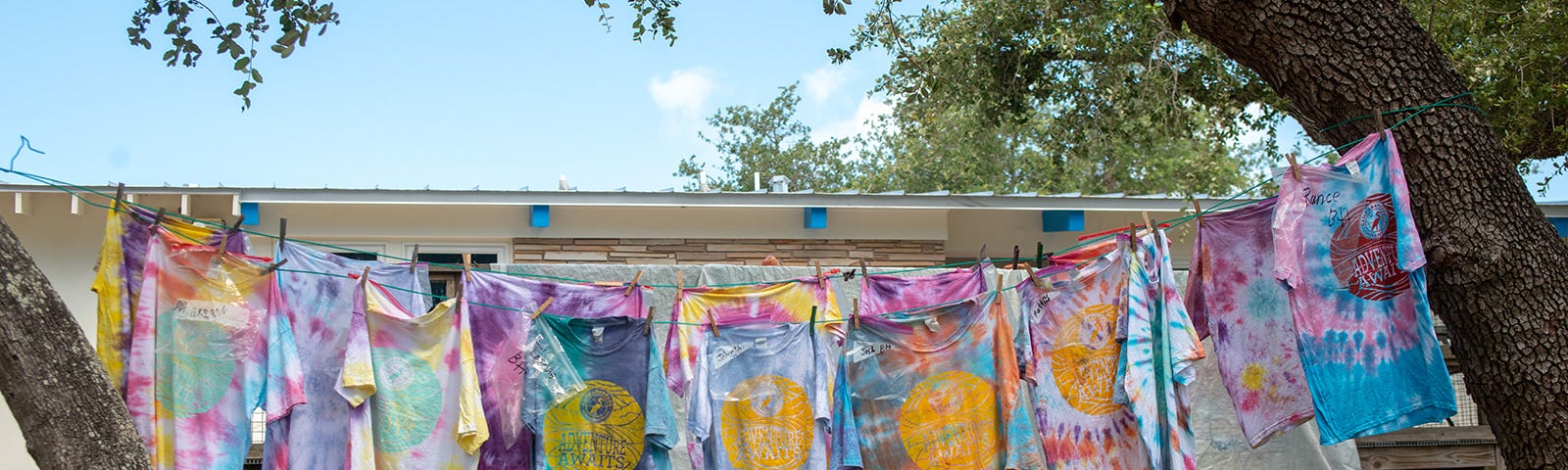 Freshly tie-dyed t-shirts hang to dry on clothes line between two trees at Camp Aranzazu
