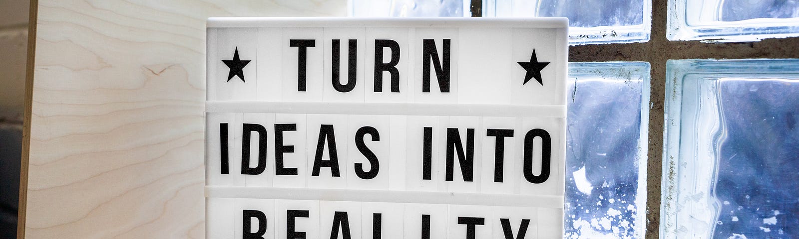 Letreiro apoiado em uma janela com o texto: transforme as ideias em realidade