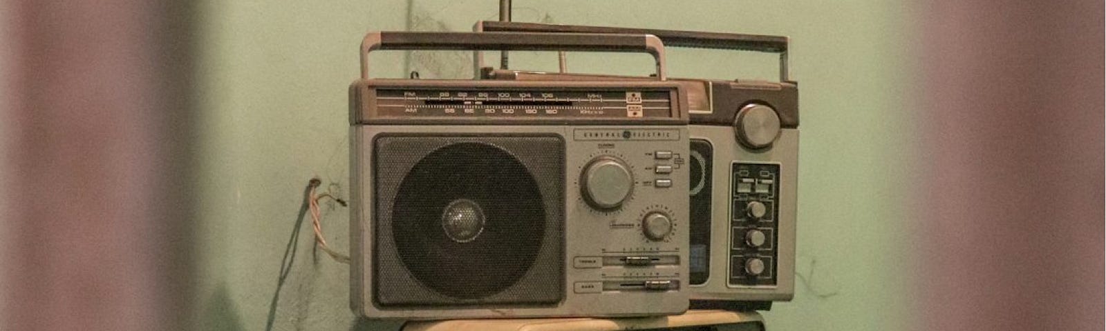 A grainy photograph of a transistor radio sitting atop an old television in a run-down room.
