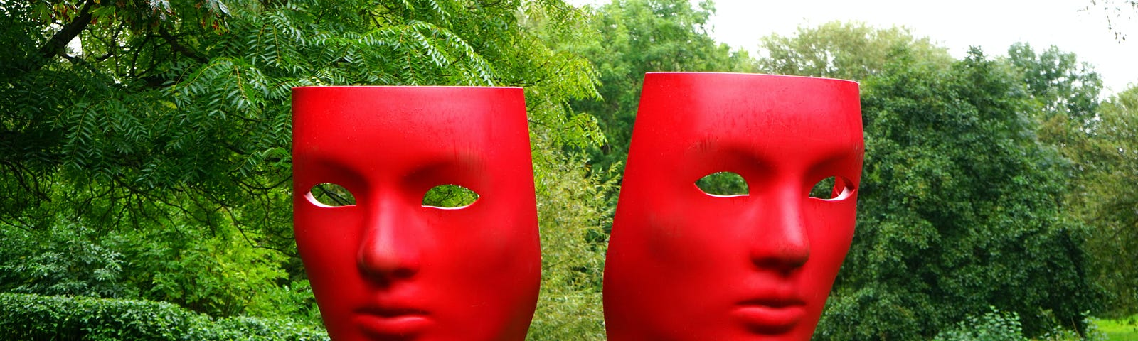 Two large red dramatic masks in a green, grassy space