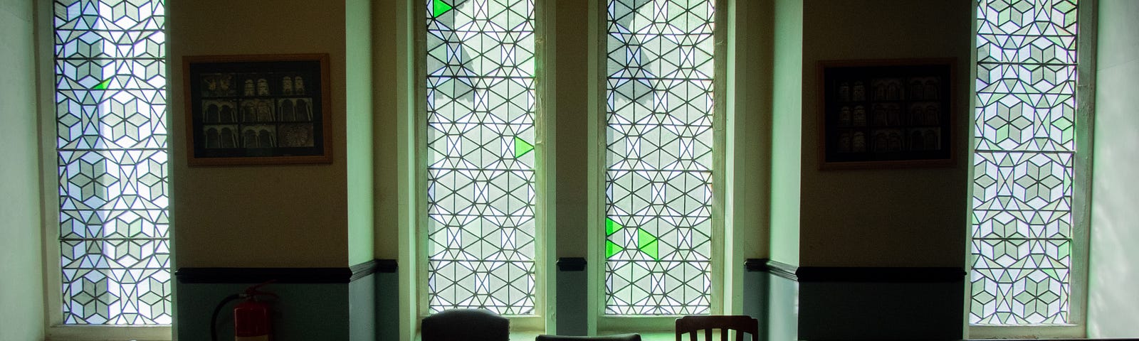 Three old chairs sit in front of a stained glass window