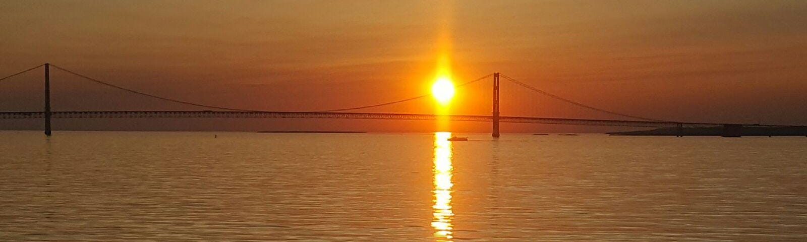 Photo of the Mackinac Bridge with the golden sun setting over the waters of Lake Huron.