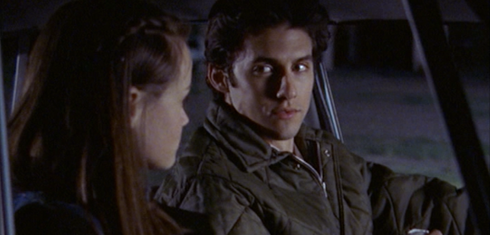 Jess Mariano and Rory Gilmore in a car at night. He is looking at her intensely and we cannot see her face as she is staring back at him.