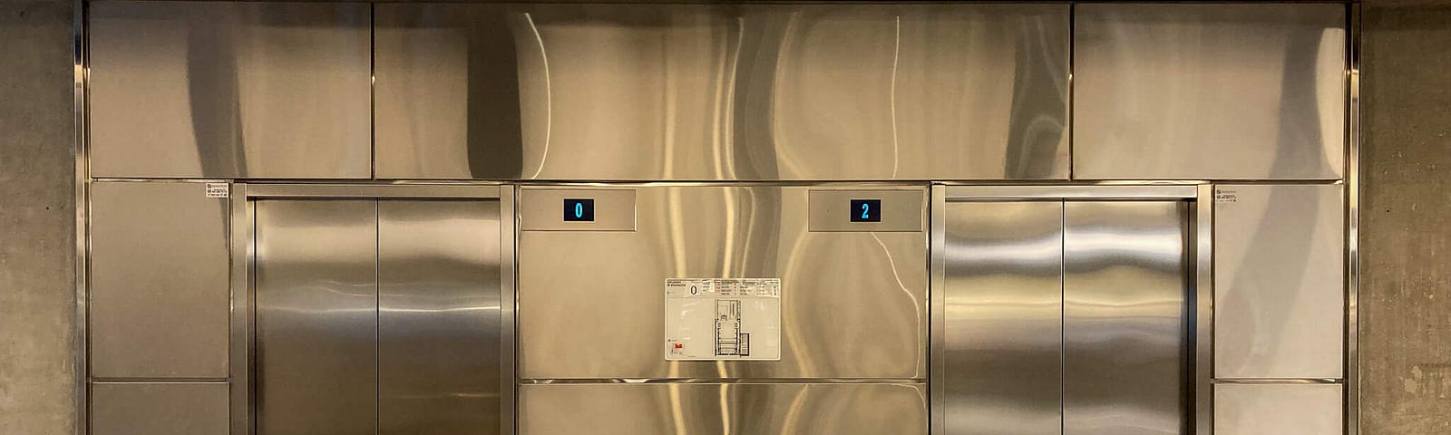 Two stainless steel elevator doors on a shiny metal wall