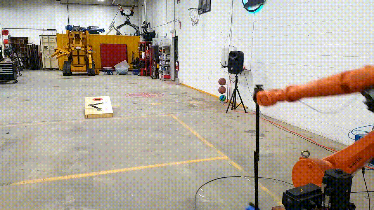 An industrial robot arm throwing a bean bag at a cornhole board.