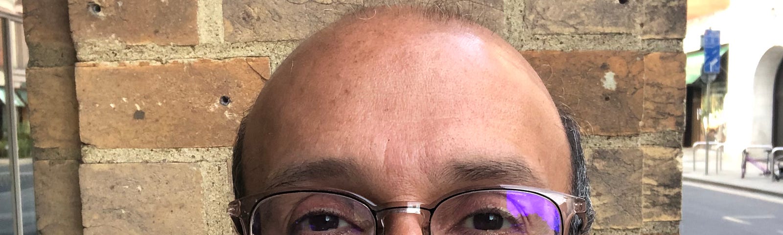 Man with glasses standing in front of brick pillar by side of road.