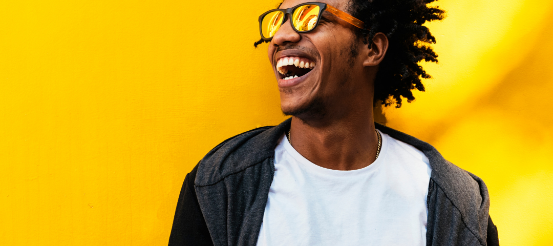 Smiling man with sunglasses against a gold background working on his phone