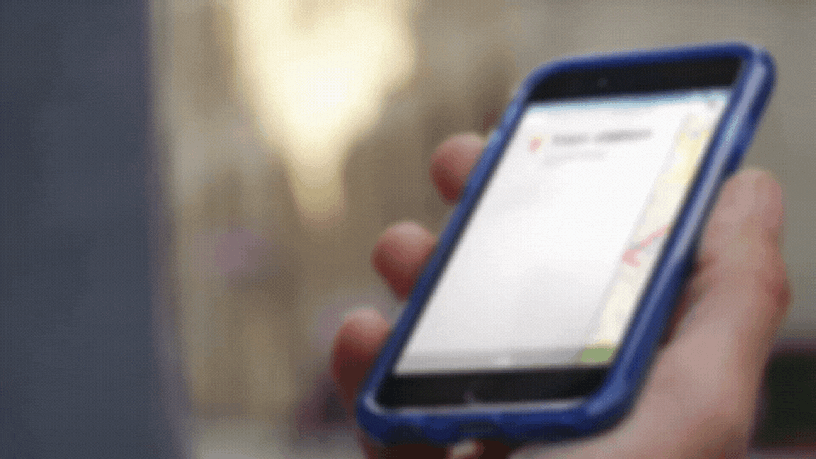 Blurred image of a hand holding a phone, with the screen displaying a transport app.