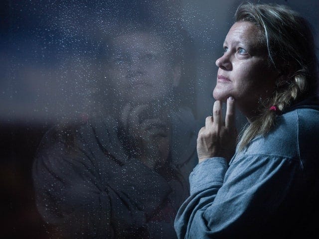 Clear glass window panel casting reflection of woman with hand touching jaw