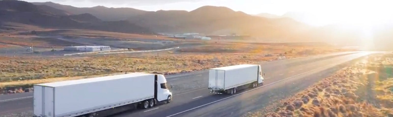 Two Tesla electric semis traveling towards the sunset.