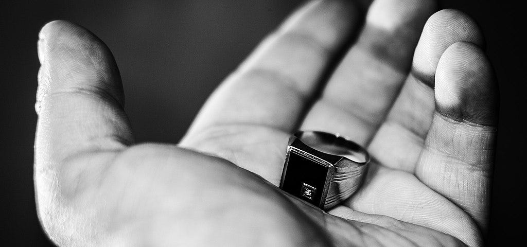 A hand holding a signet ring with black onyx plate