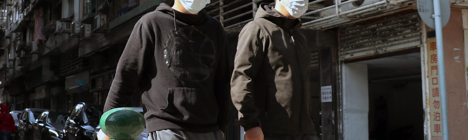 Two men walk together down the street with COVID-19 masks on.