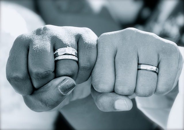 Two married people bumping fists sideways, showcasting their rings