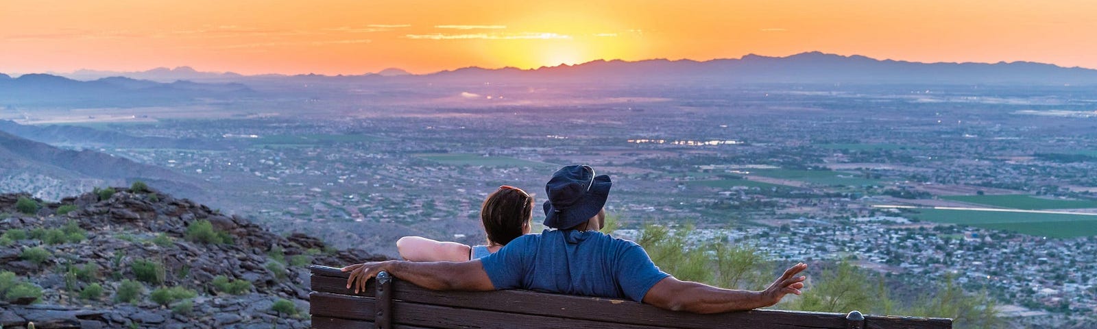 Two people sitting on a bench looking at the sunset.