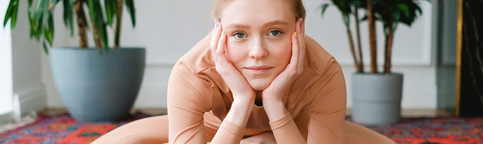 A woman sitting on a yoga mat, with her face in her hands.