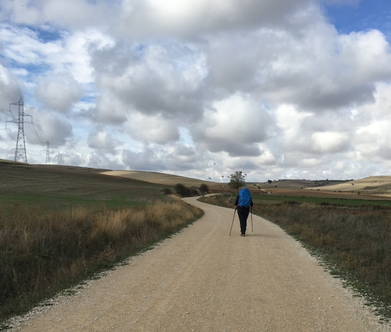 Camino de Santiago — -a walker walks a long gravel track, with clouds above.