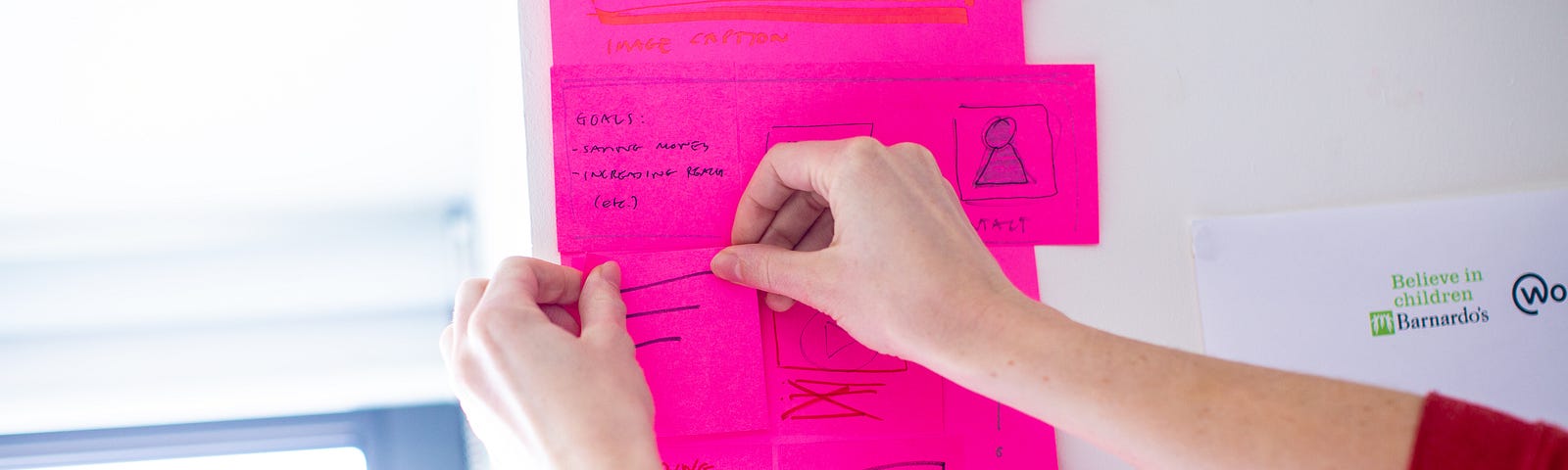 A person sticking notes up on the wall. The notes contain ideas from a Products and Services team workshop.