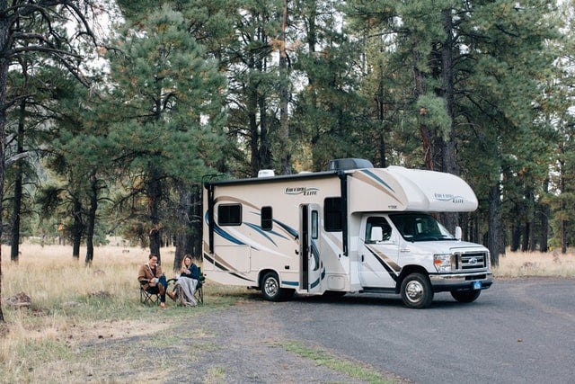 A couple are sitting in a forest enjoying the scenery. Their RV is parked right next to them.