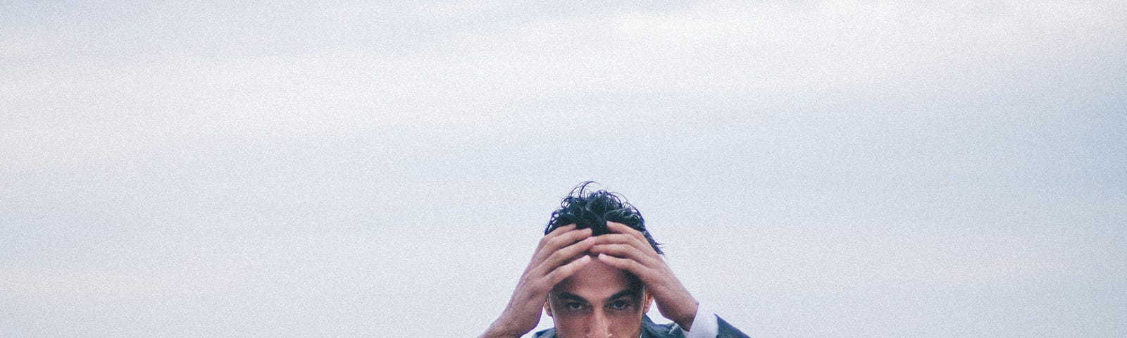 An adult man is above his waist in turbulent water. His hands are holding his head and he looks scared and troubled.