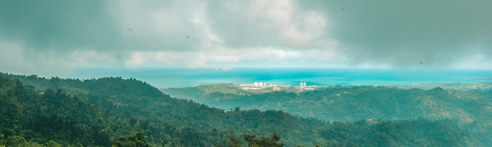An wide shot of Puerto Rico’s protected forests as clouds billow overhead and the sea sprawls out in the distance.