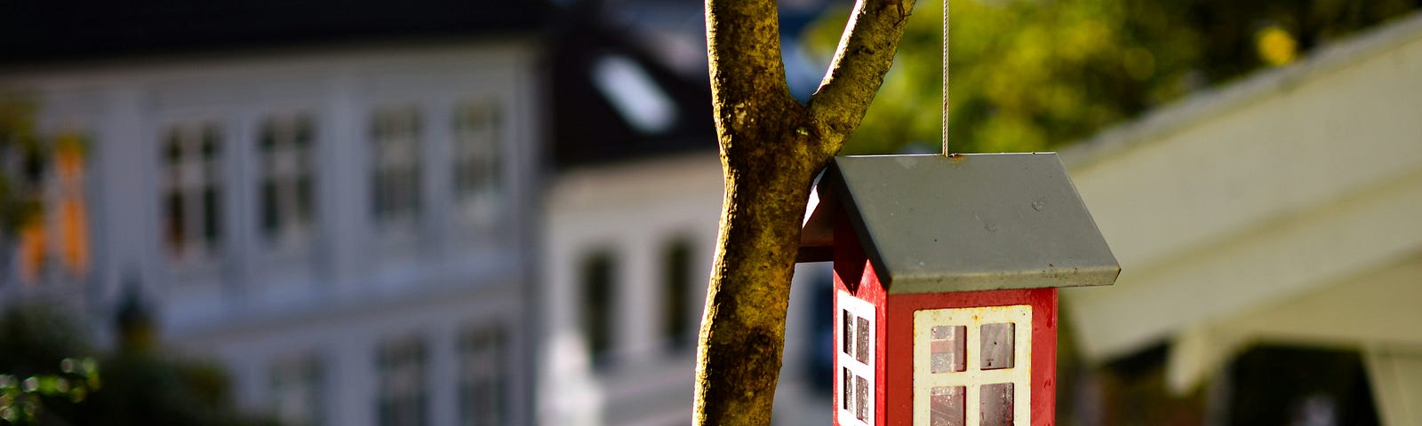 Small red birdhouse in front of a large white house