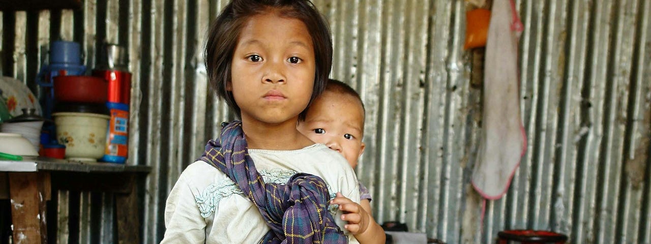 A young girl carrying a smaller child on her back