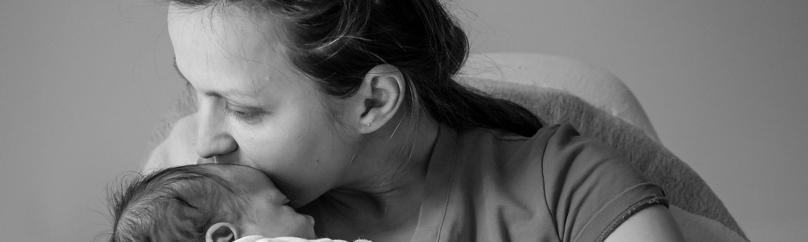 Grayscale photo of a woman holding a baby in her arms with her face to the baby’s forehead.