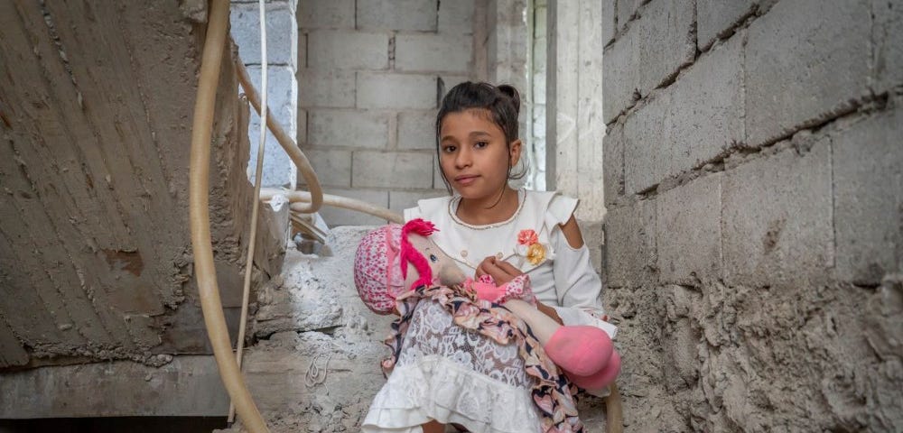 Tolvåriga Amina sitter med en docka i knäet i ett raserat stentrapphus.