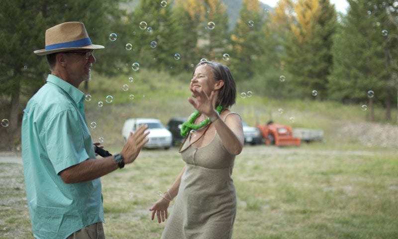 A white man and white woman standing in a field playing with bubbles