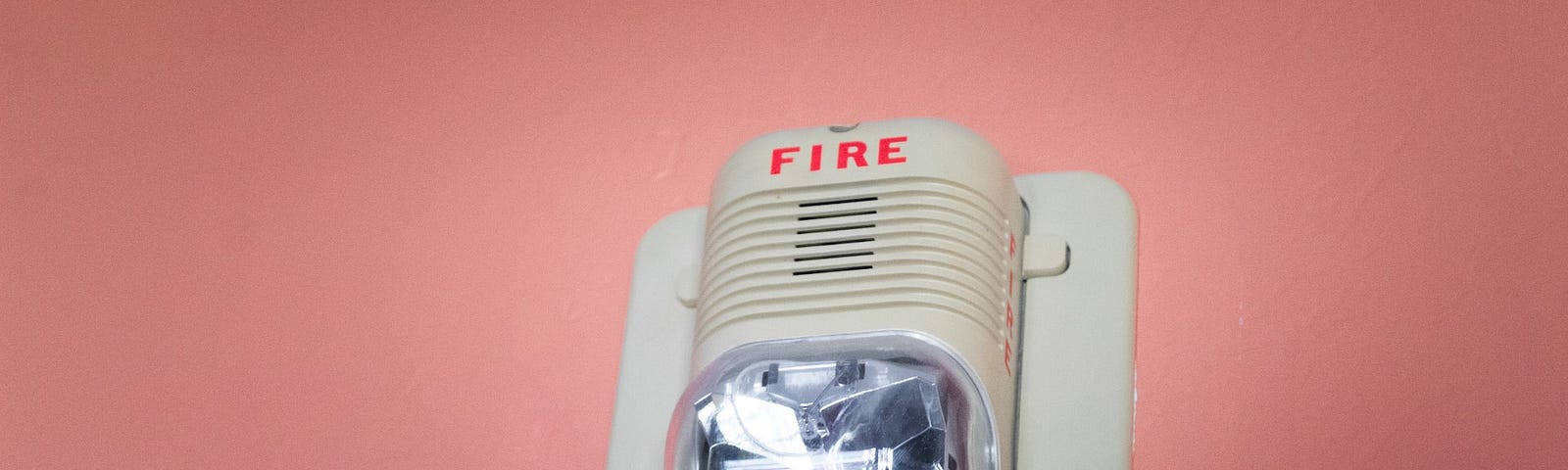 A fire alarm alert with a speaker and a flashing light mounted to a coral-colored wall