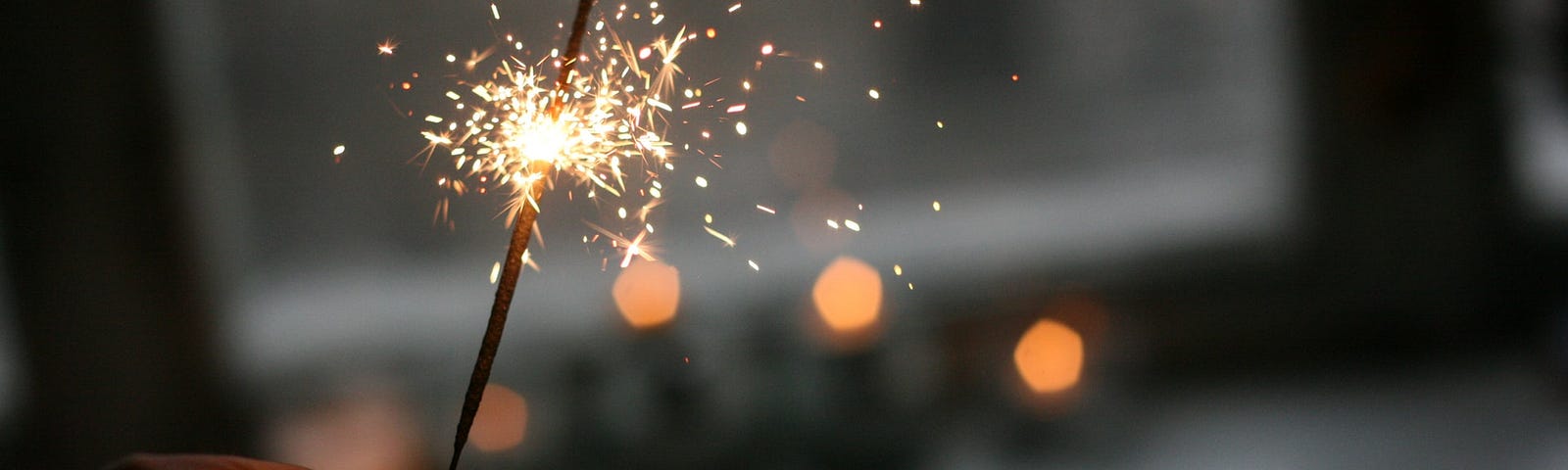 Hand holding out a lit sparkler in a dark area