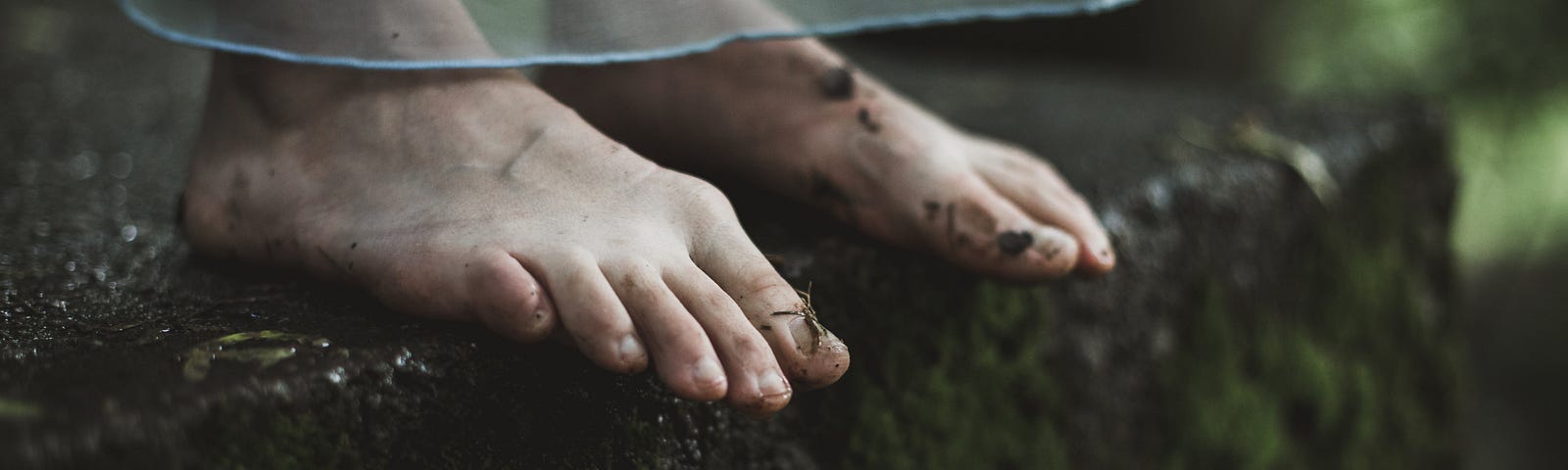 woman’s bare feet on the edge of a mossy, gray and green ledge