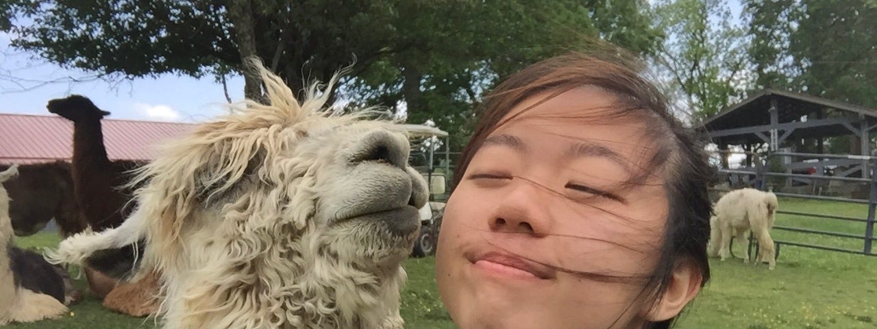 A photo of Lynn with a llama, both of them have their eyes closed, enjoying a breeze
