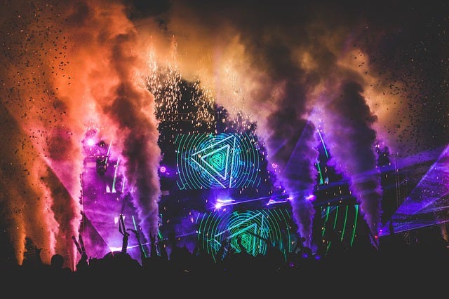 Festival with coloured light display and smoke machines, lasers against night sky with the silhouettes of the audience in the foreground