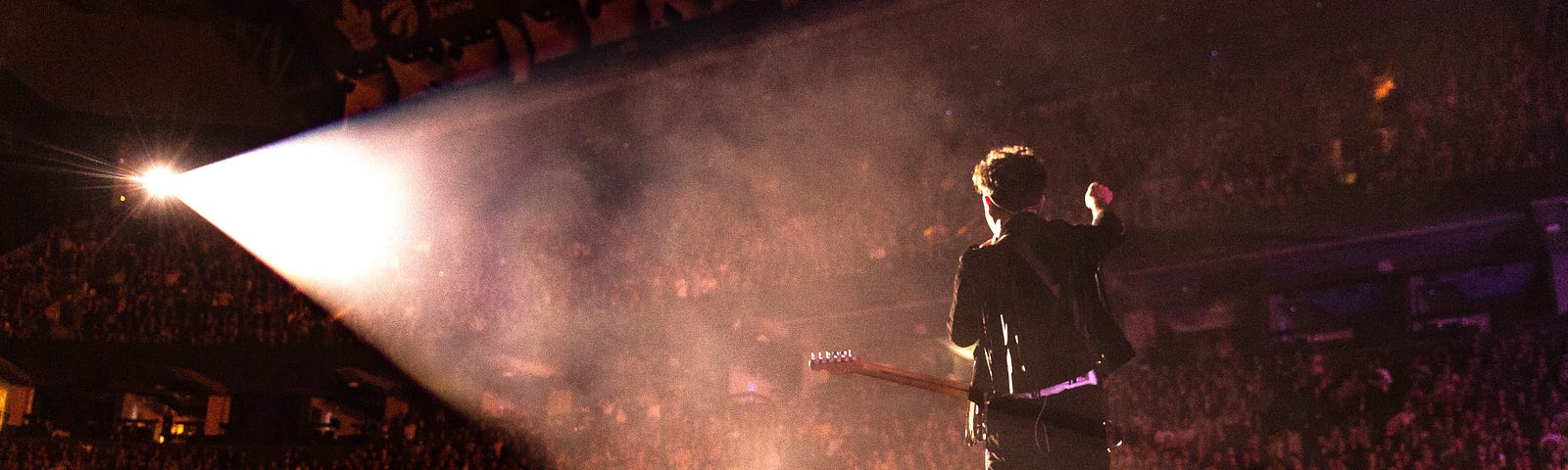 guitar player standing alone on an enormous filled stadium stage