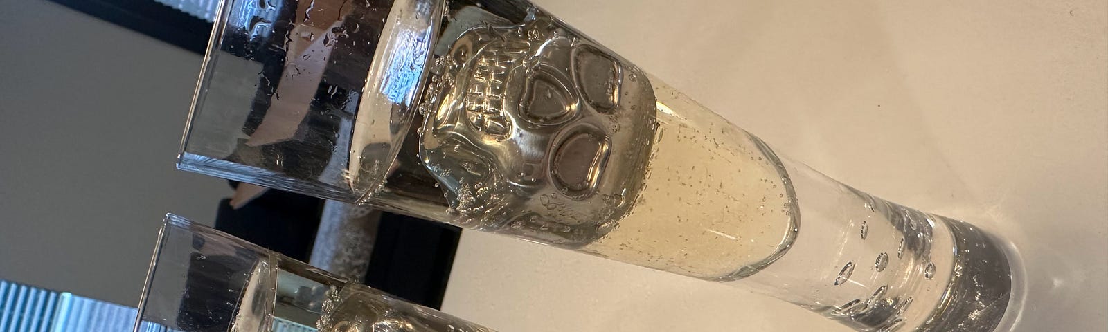 Two full champagne flutes with skull-shaped whiskey stones floating in them.