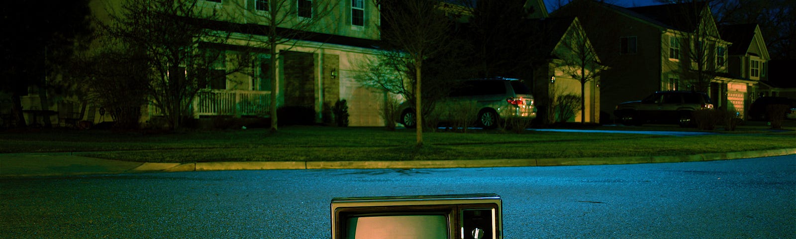 An old box-style TV on the ground in the middle of a suburban street