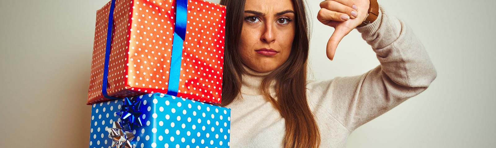 A woman holding two Christmas presents and giving them a thumbs down gesture because she hates them