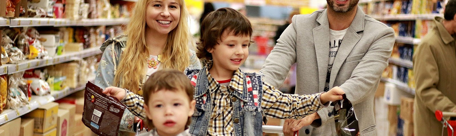 A family pushes a grocery cart and smiles.