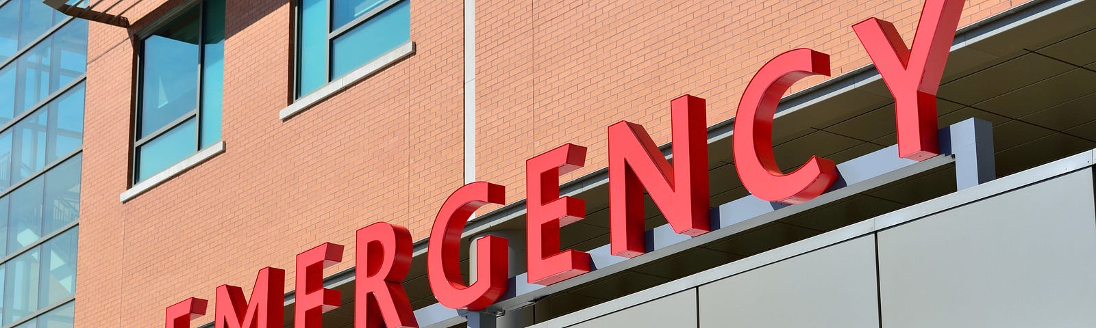An emergency room outdoor signage with the word “EMERGENCY” in red capital letters