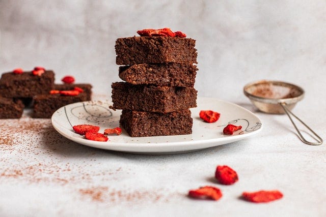 A small plate stacked with 4 brownies. Dried strawberries decorate it along with sprinkled cocoa.