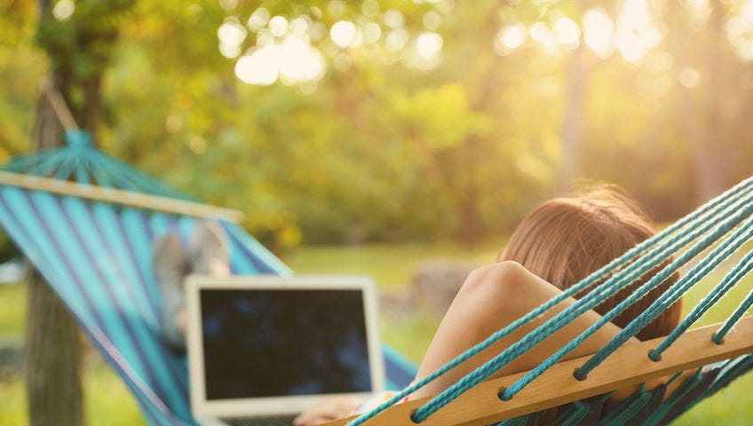 a person lying in a hammock in a wooded area using a laptop