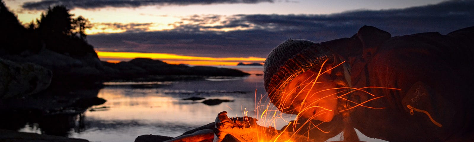 Woman tending to a bonfire by the mountains and the sea