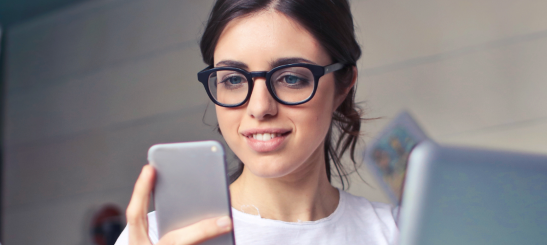 Woman wearing glasses and a white t-shirt looking at her phone