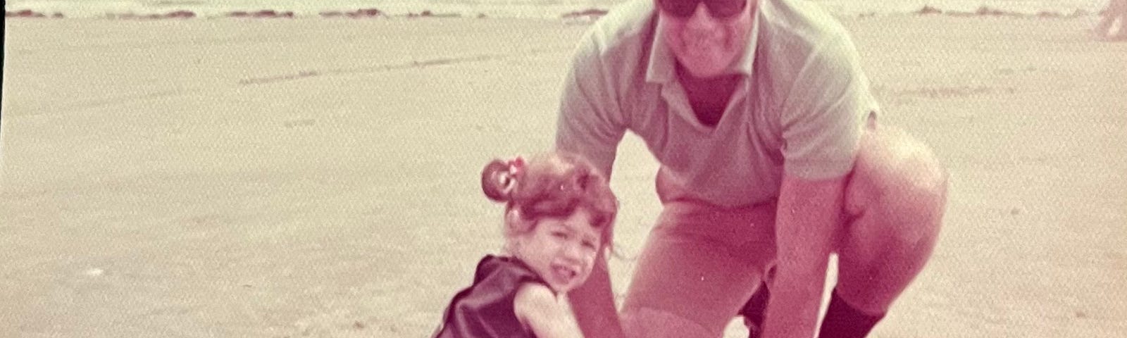 An old faded photo of a little girl and her dad at the beach.