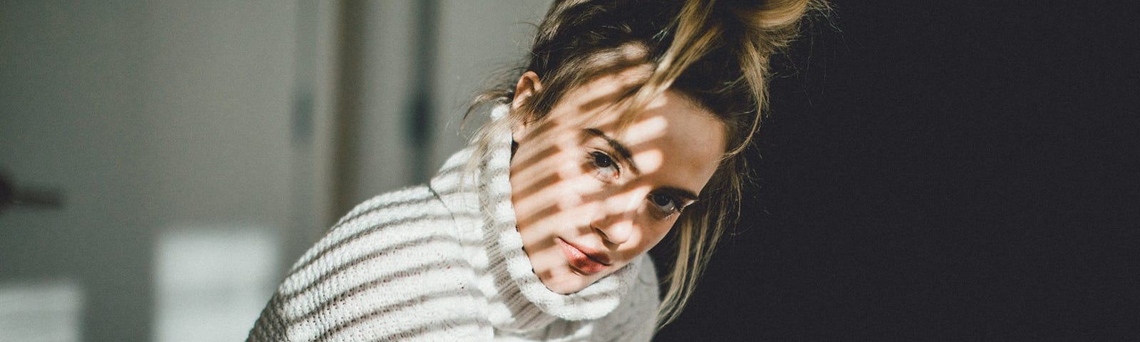 A woman with a serious gaze and a messy bun stares at the camera behind reflected slants of light.